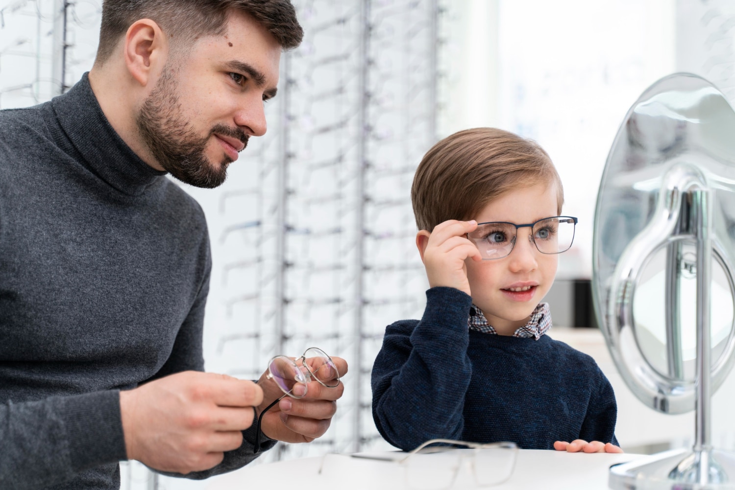 Jeune homme opticien aidant un jeune enfant à choisir des lunettes en le faisant essayer